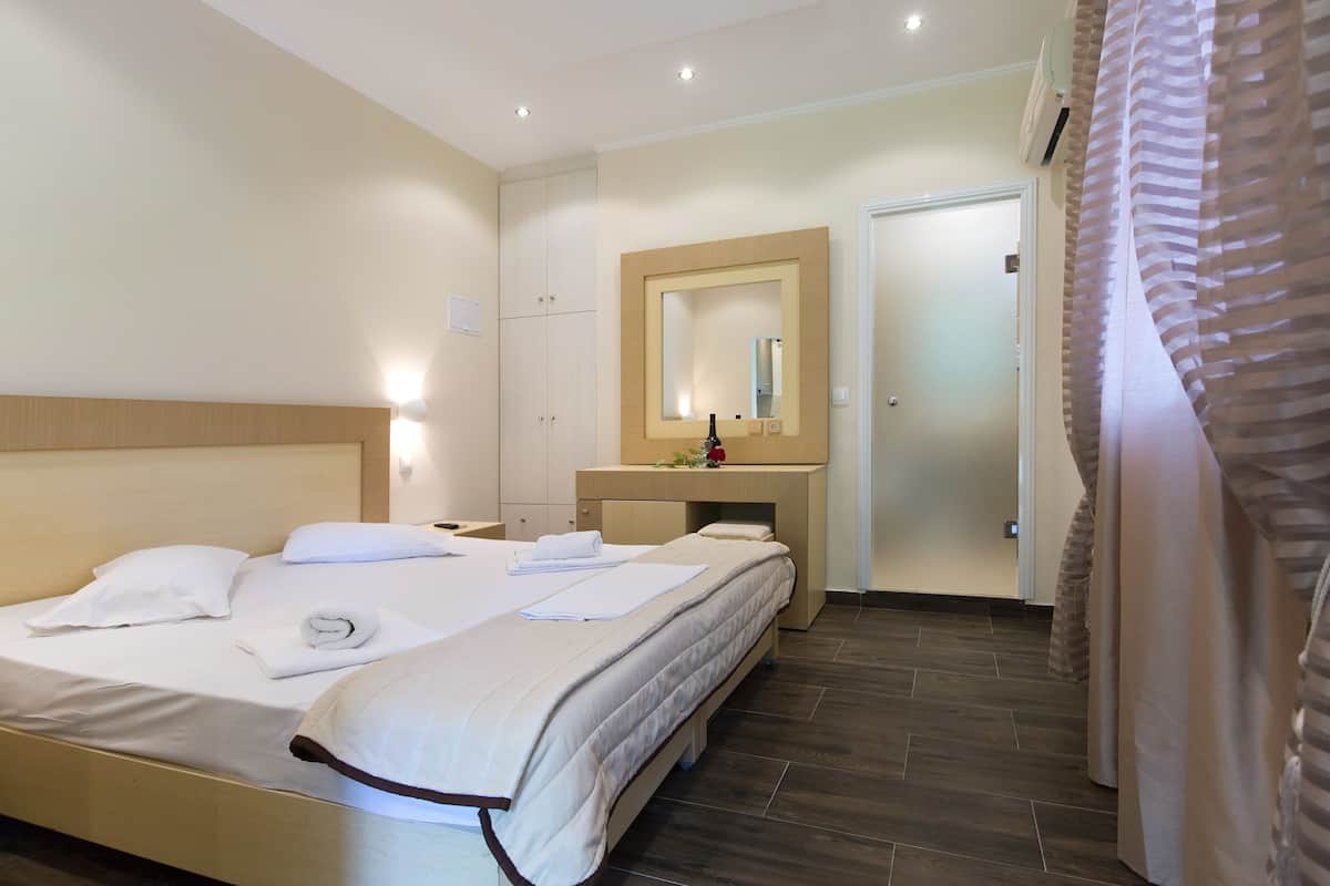 A hotel room with a bed, bedside table, a mirror, a small desk with a chair, and a door.