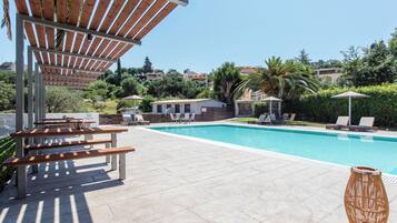 Zona de piscina con bancos de madera, sillones de descanso y sombrillas.