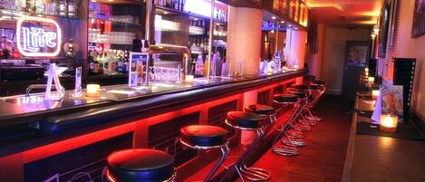 A bar area with stools, a minibar, and a neon sign.