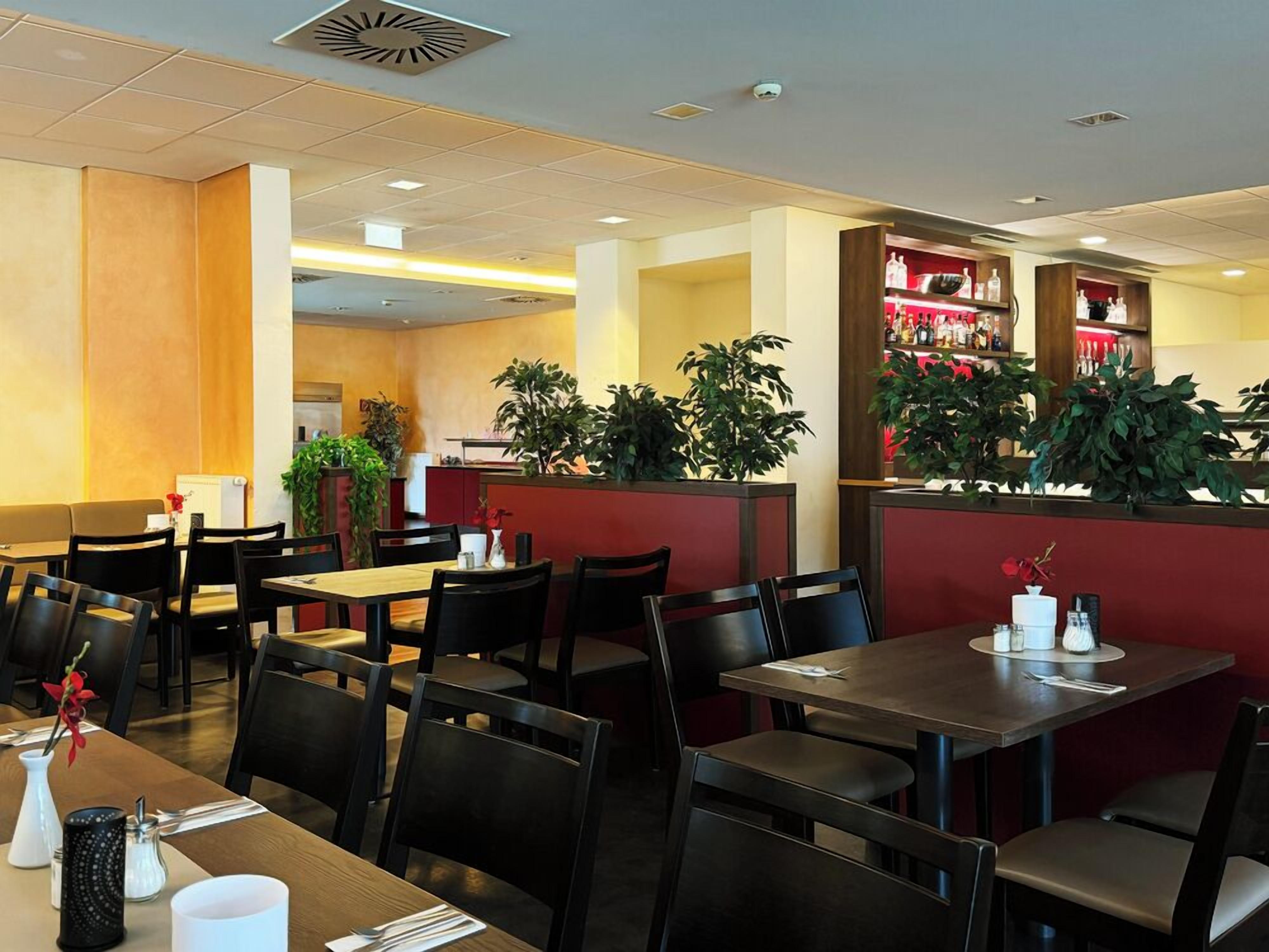 A restaurant interior with tables and chairs, a counter with a beverage display, and potted plants.