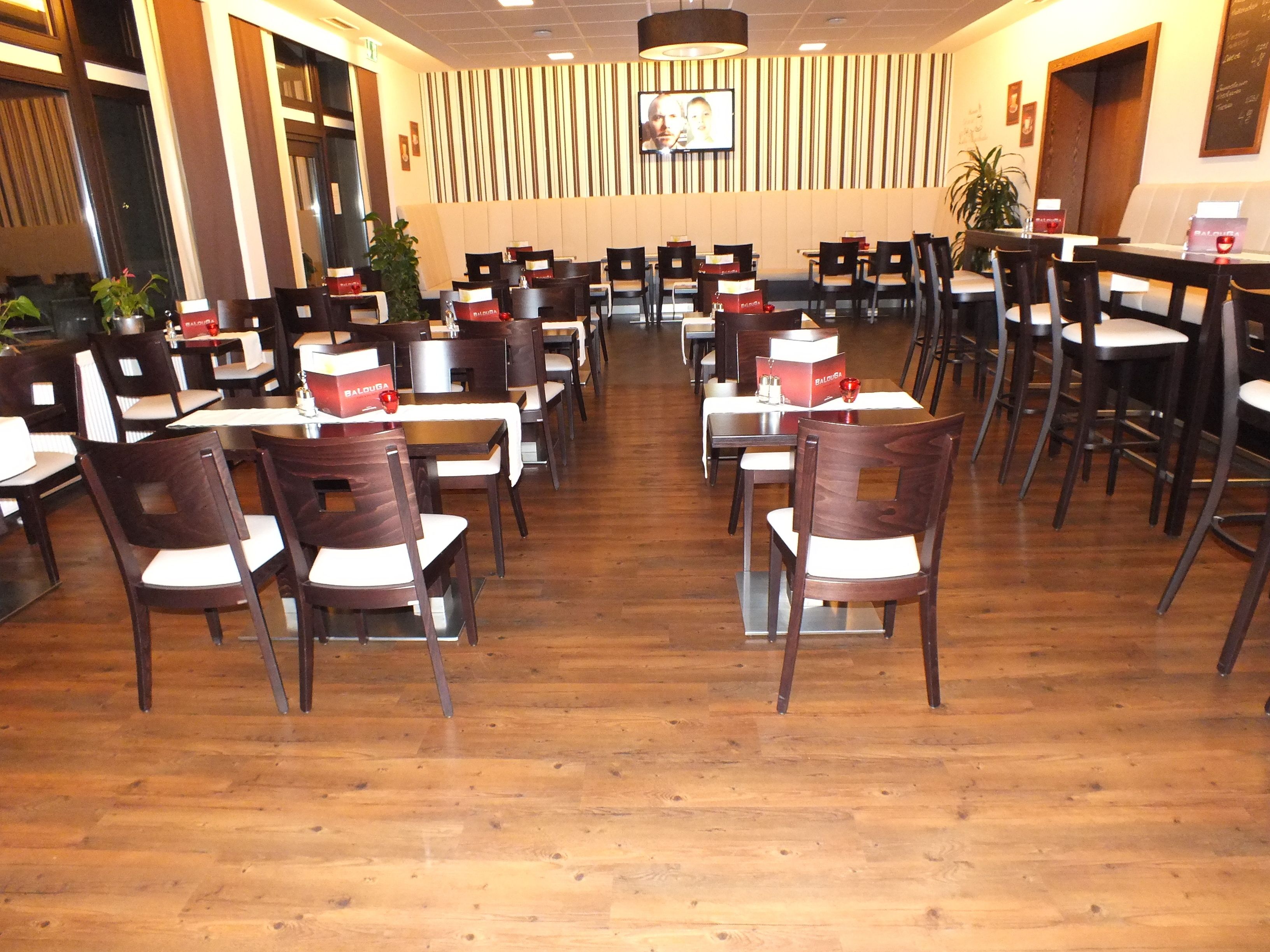 A restaurant with multiple tables and chairs, wooden flooring, and a television mounted on the wall.