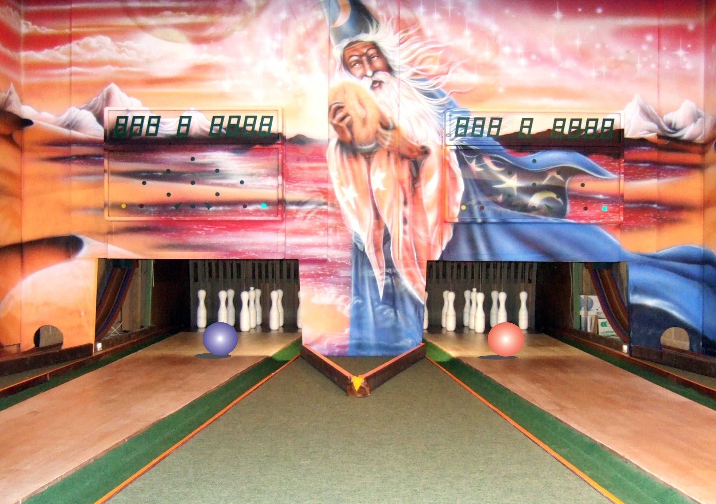 A bowling alley with a large mural of a wizard on the wall, bowling pins, and a bowling ball on the lane.