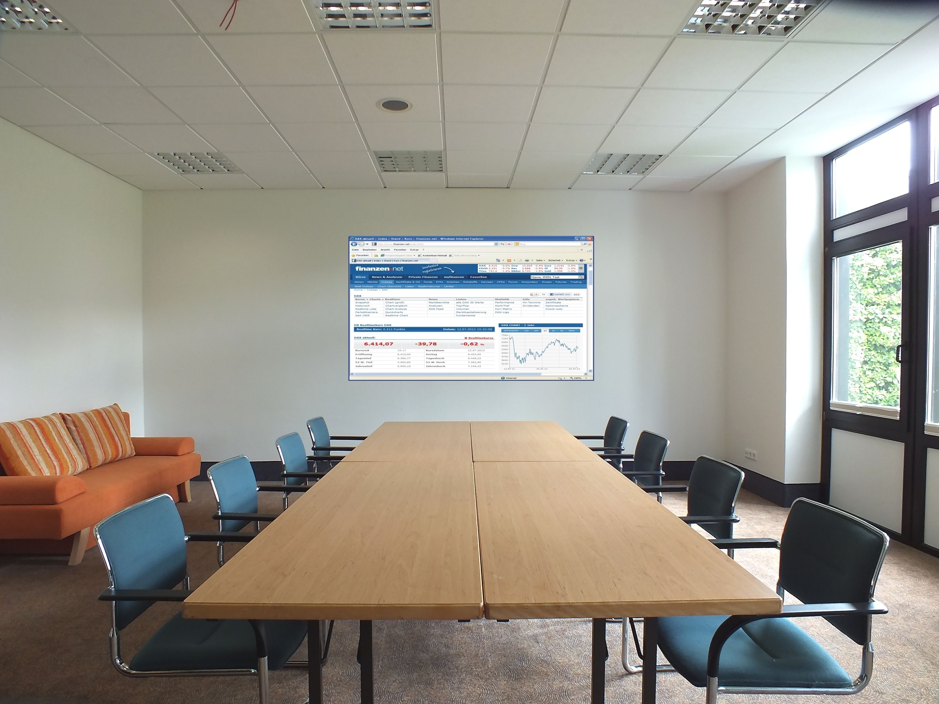 A conference room with a long table, blue chairs, an orange couch, and a large screen displaying financial data.