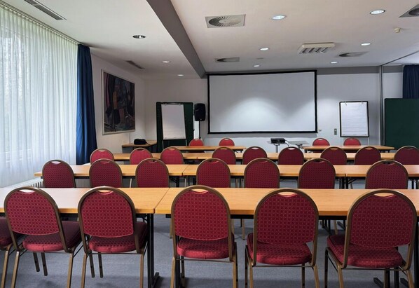 Una sala de conferencias con varias mesas y sillas, una pantalla de proyector y una pizarra.