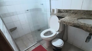 Casa de banho com sanita, chuveiro e um tapete vermelho.