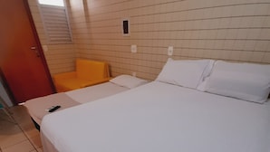 Quarto de hotel com uma cama, uma cadeira, uma janela pequena e uma porta.