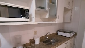 Cozinha com armários brancos, bancada de granito, micro-ondas, liquidificador e pia.