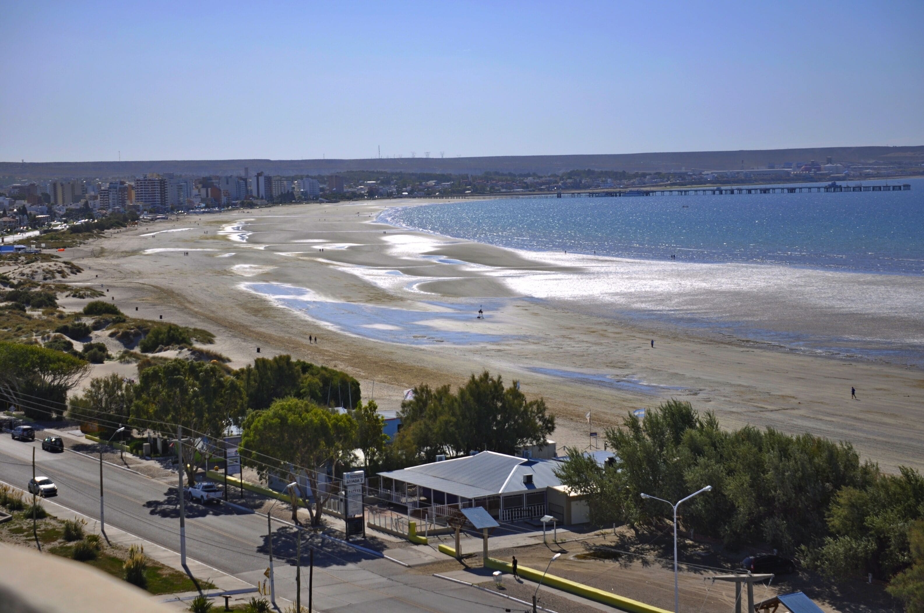 A coastal road with a beach and a pier in the background.