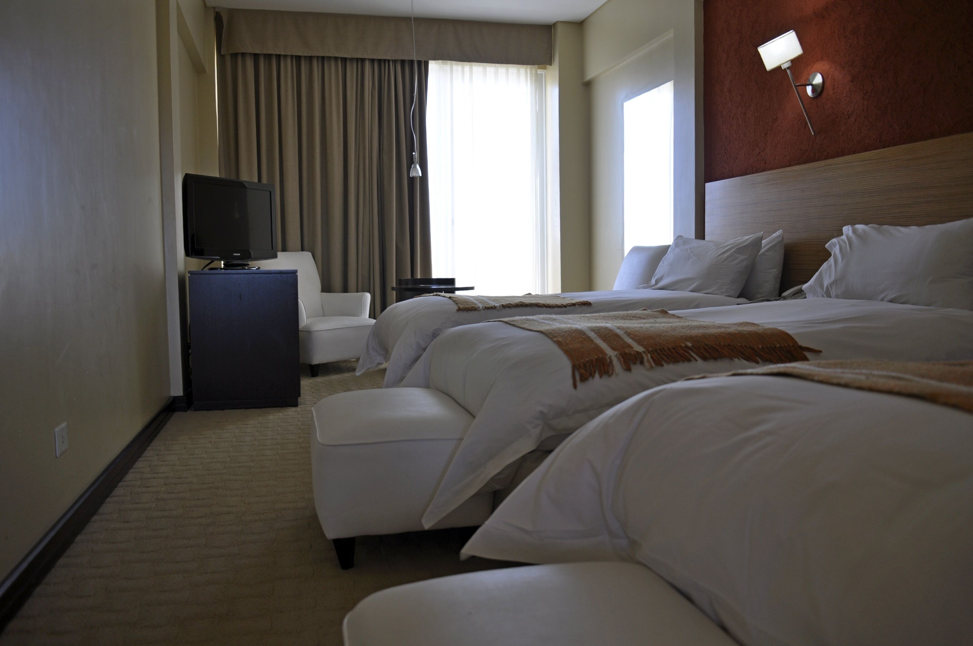 Ein Hotelzimmer mit zwei Betten, einem Fernseher, einem Schreibtisch und einem Fenster mit Vorhängen.