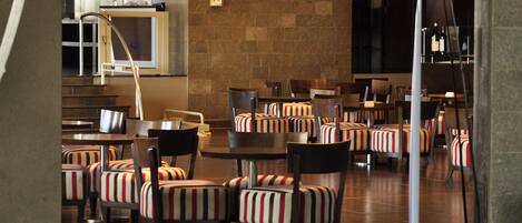 A spacious restaurant with striped upholstered chairs and tables, a brick wall, and a staircase leading to an upper level.