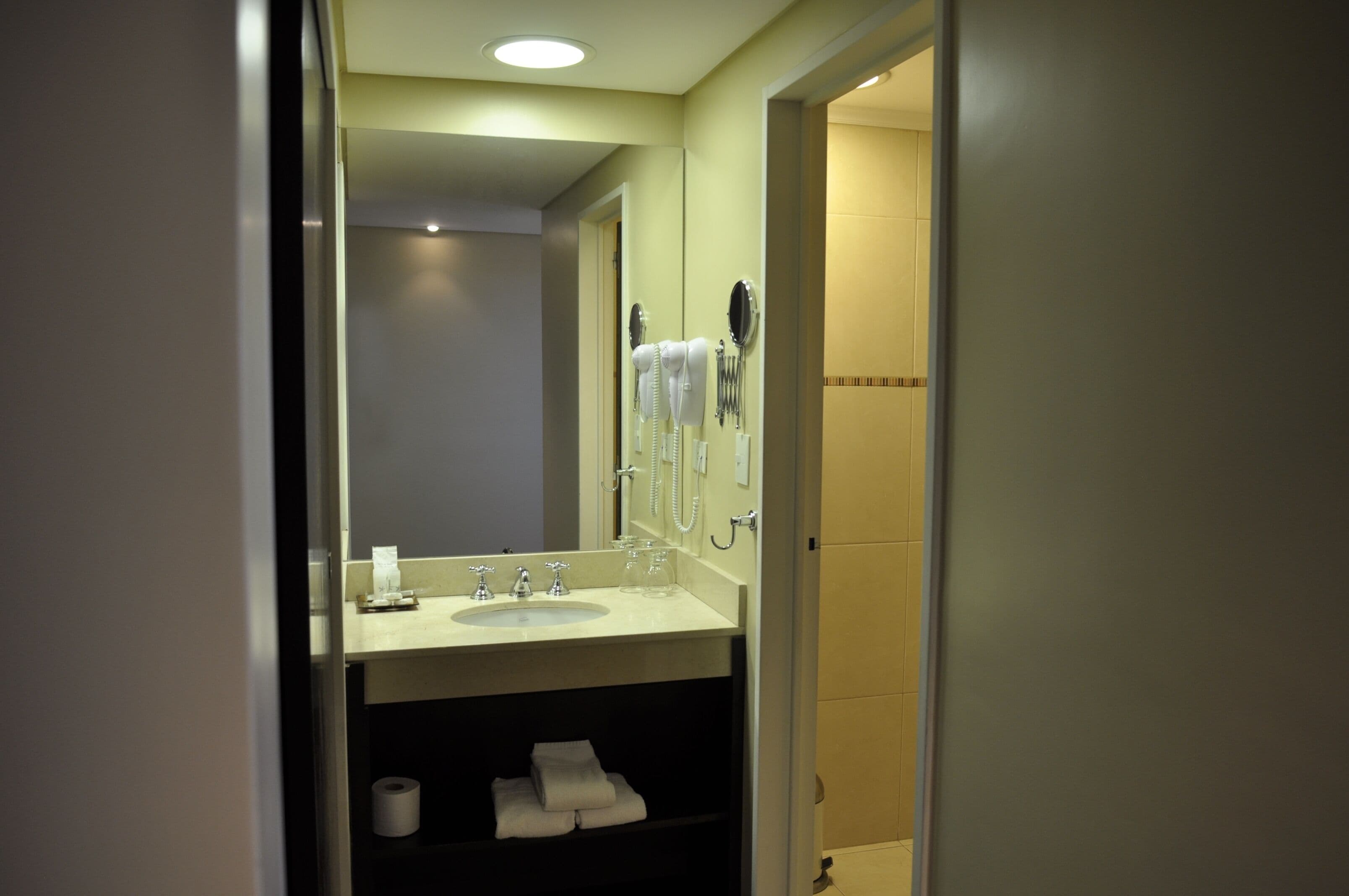 A bathroom with a sink, mirror, towel rack, and toilet paper.