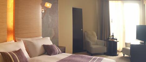 A hotel room with a large bed, a sitting area with a chair and a small table, and a television.