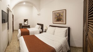A hotel room with two beds, a desk, a chair, a telephone, and a painting on the wall. - Hotel La Plazuela (Popayán)