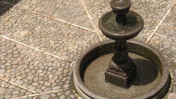 A stone fountain with a central spout and a smaller spout on top, surrounded by a circular stone base.
