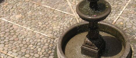 A stone fountain with a central spout and a smaller spout on top, surrounded by a circular stone base.
