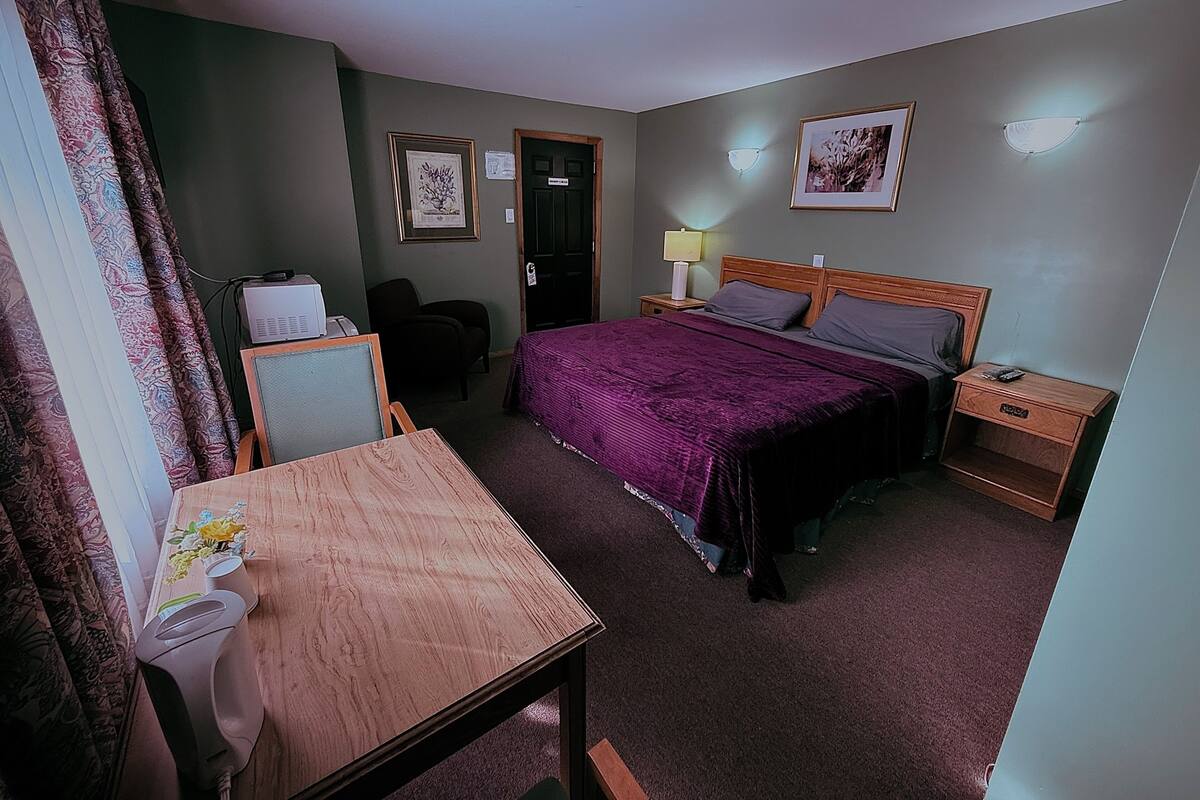 A hotel room with a bed, bedside tables, a desk with a chair, a lamp, and two framed pictures on the wall.
