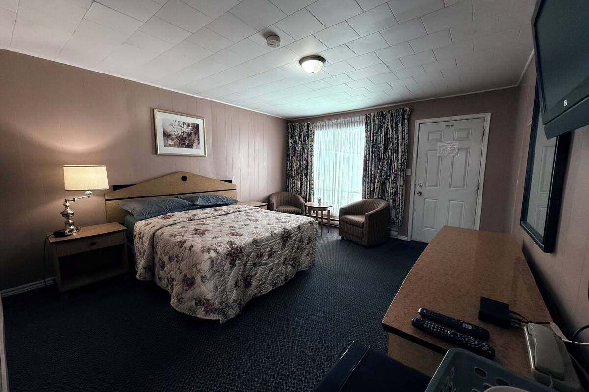 A hotel room with a bed, a desk, a chair, a lamp, a television, and a door.