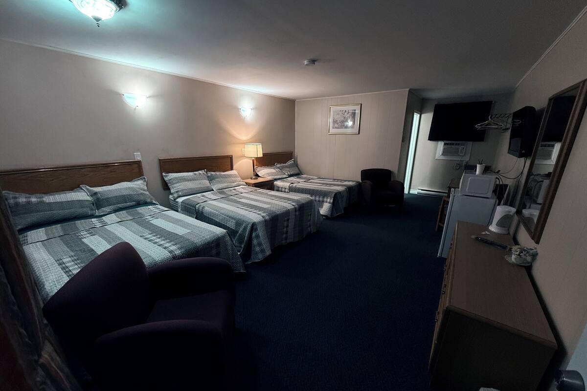 A hotel room with three beds, a desk, a chair, a lamp, a television, and a microwave.