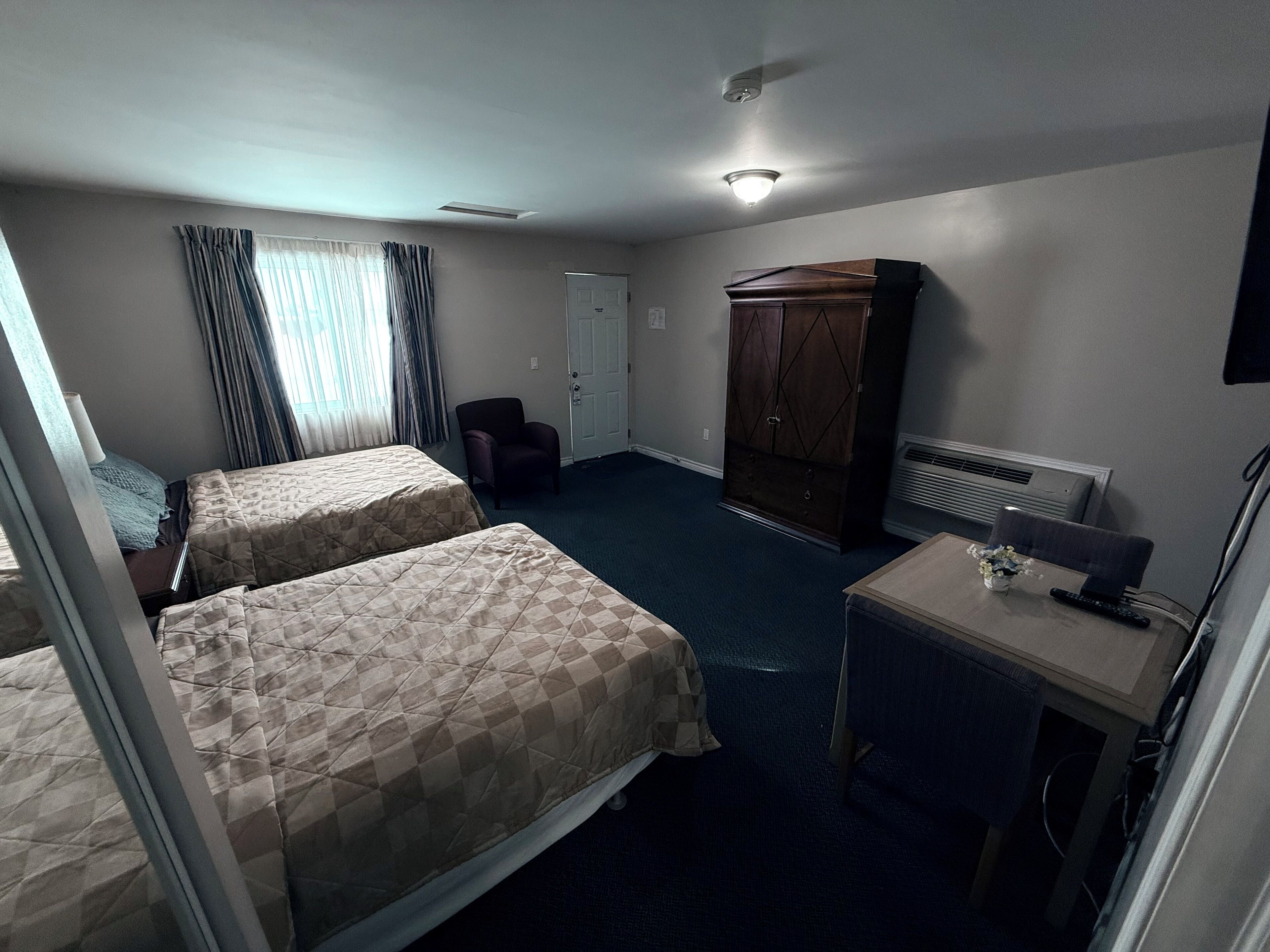 Habitación de hotel con dos camas, una silla, un escritorio con lámpara, un armario y un radiador.