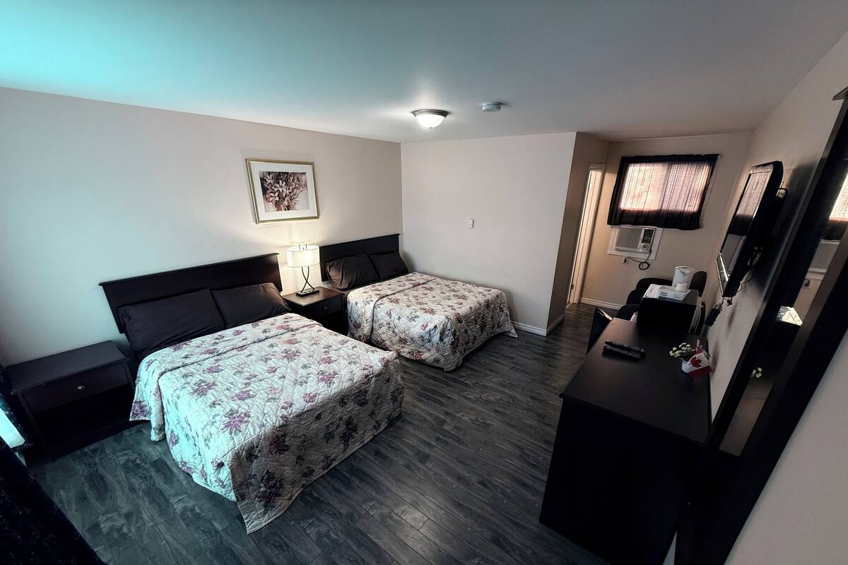A hotel room with two beds, a desk, a chair, a mirror, and a window with curtains.