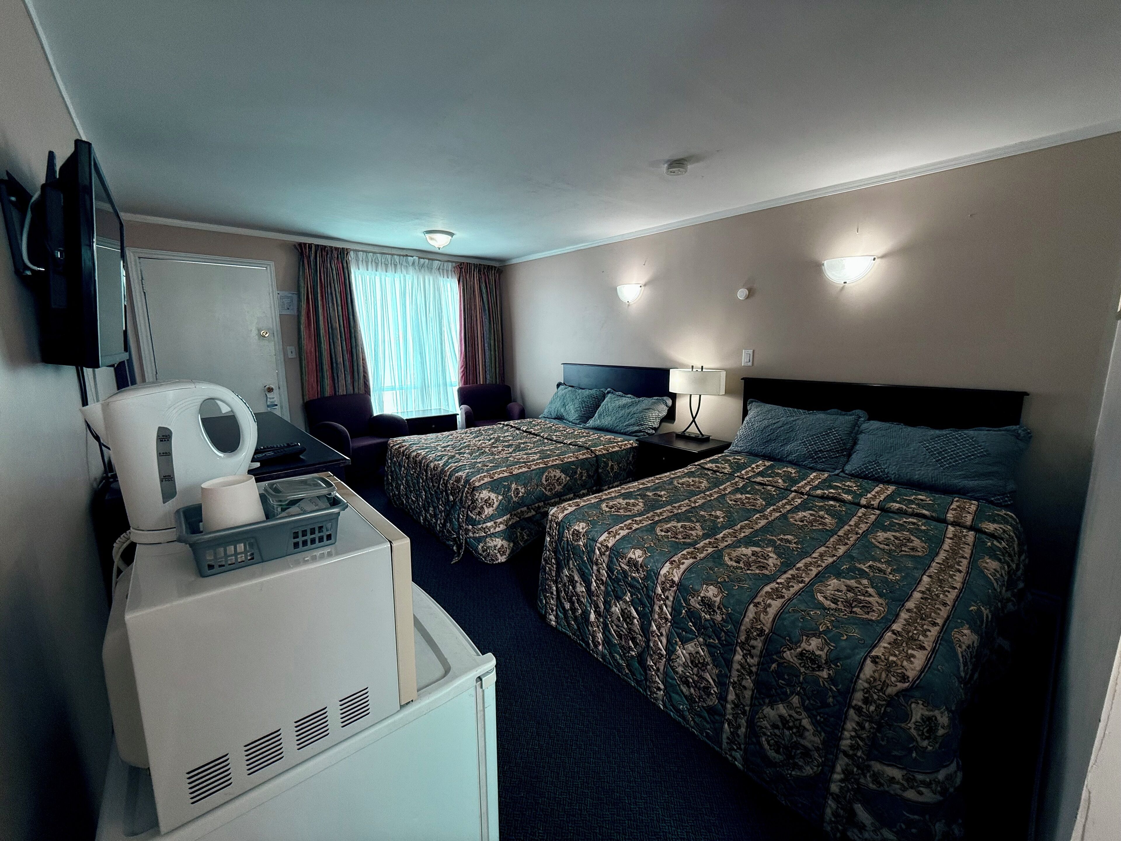 A hotel room with two beds, a desk with a computer, a coffee maker, and a TV mounted on the wall.