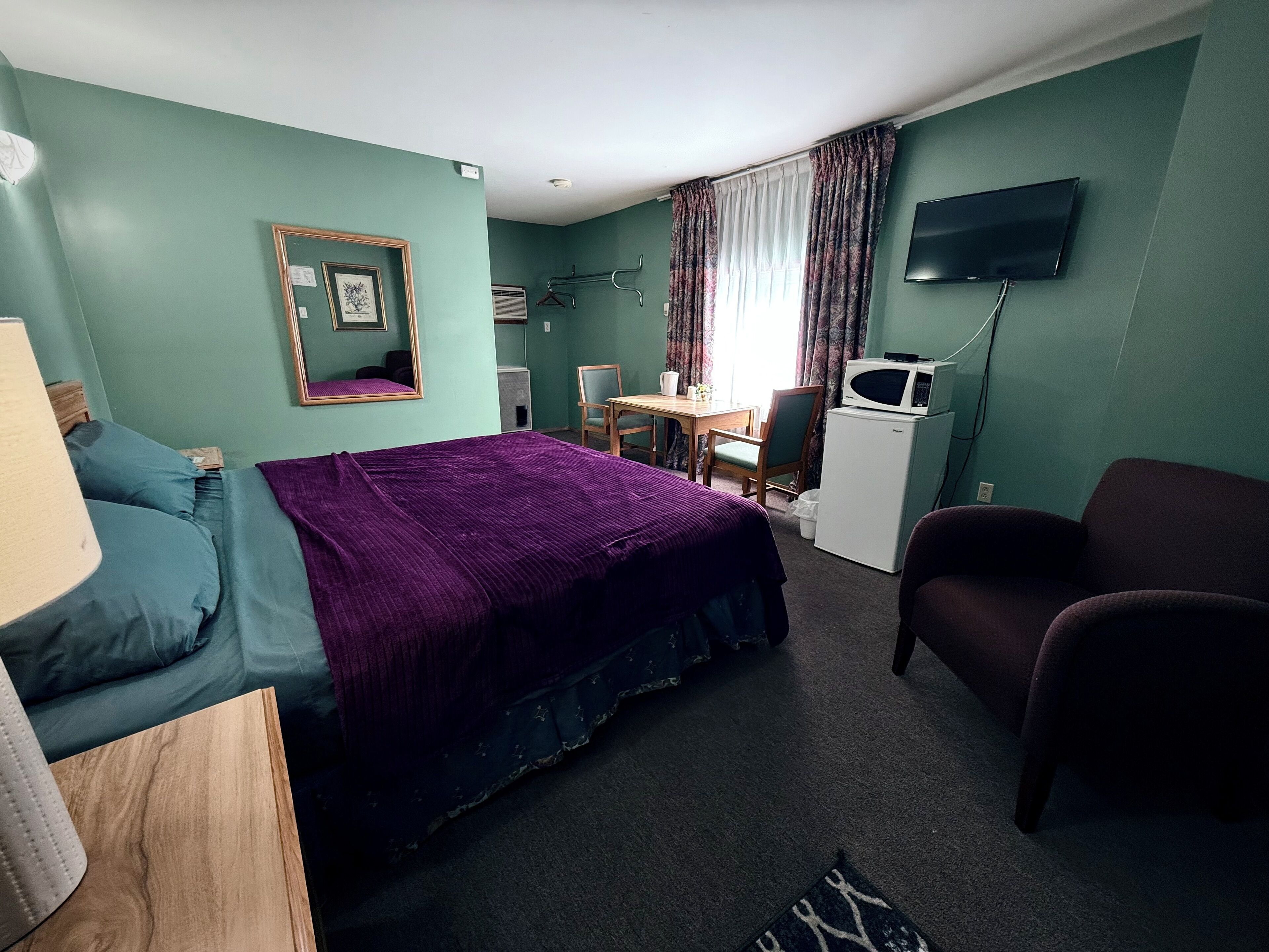 A hotel room with a bed, a desk, a chair, a television, and a microwave.