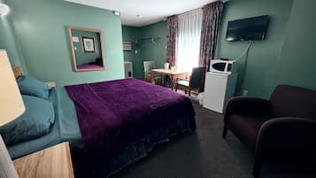 A hotel room with a bed, a desk, a chair, a television, and a microwave.