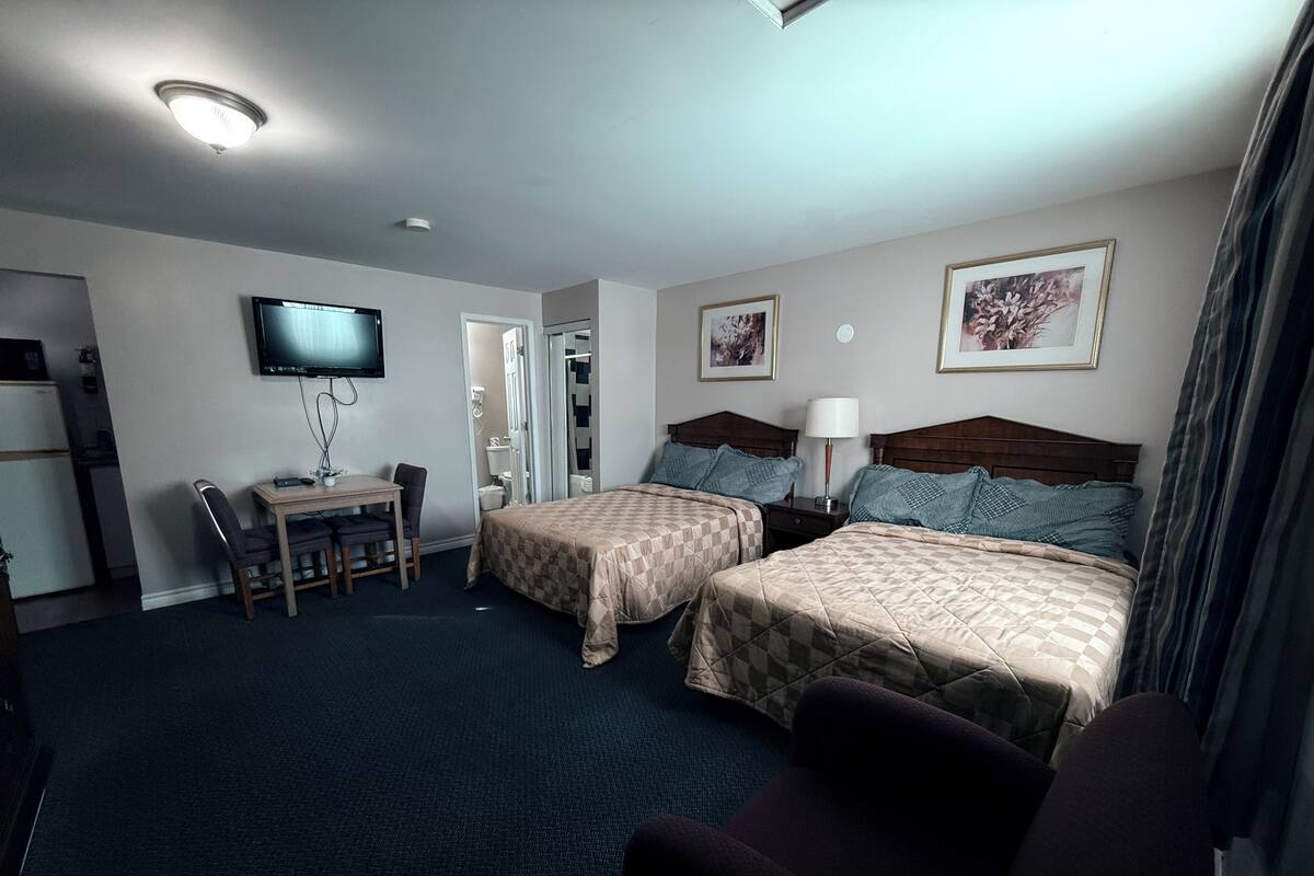 A hotel room with two beds, a desk with a chair, a television, and a small kitchenette.