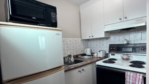 A compact kitchen with white cabinets, a black microwave, a white refrigerator, a stove, and a sink. - Guest Inn (Quinte West)