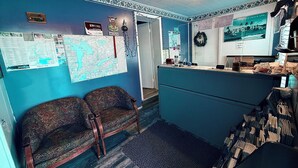 A room with a blue wall, a map, a bulletin board, two patterned chairs, a desk, and a shelf with books. - Guest Inn (Quinte West)
