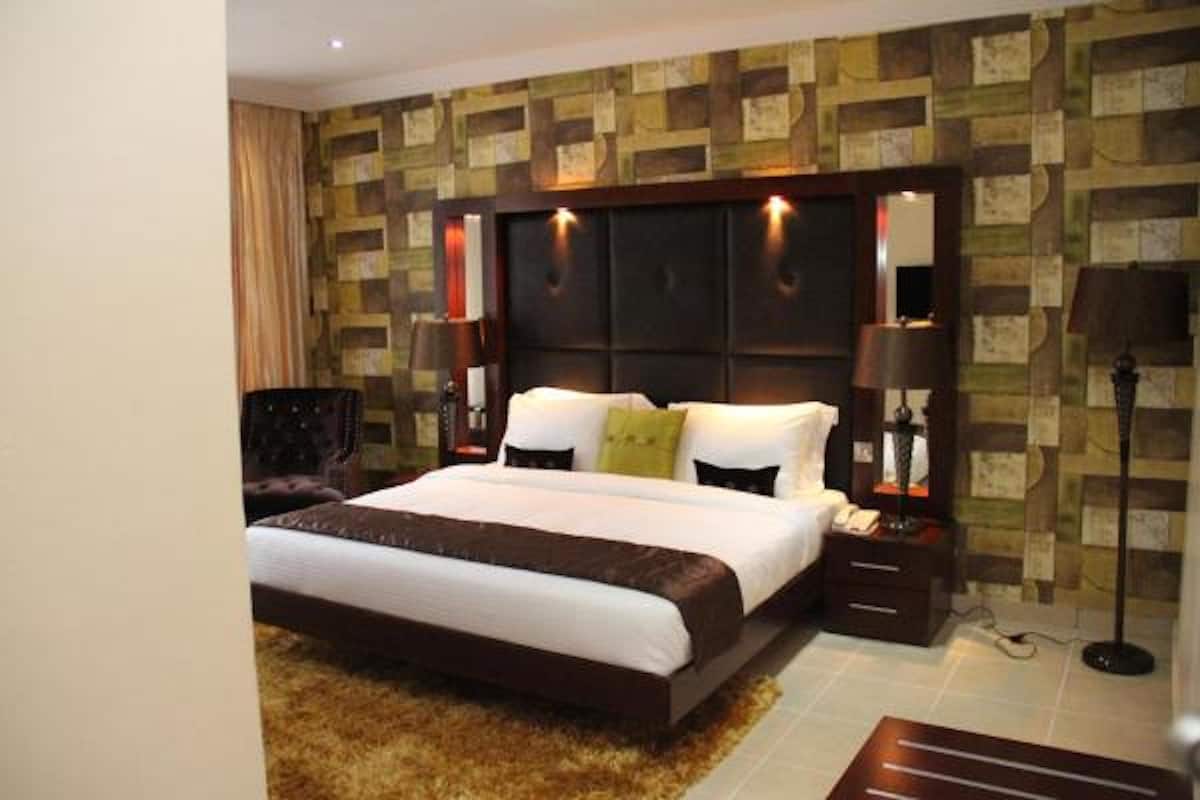 Ein Hotelzimmer mit einem großen Bett, einem dunklen Kopfteil und Wandtapete mit Muster.