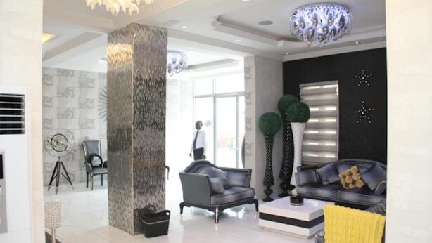 A modern living room with a large column, a sofa, a coffee table, and a chandelier. - Palazzo Dumont Hotel (Lekki)