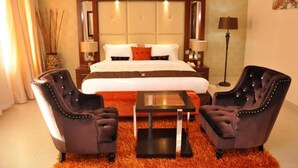 A hotel room with a large bed, two armchairs, a small table, and a nightstand with lamps. - Palazzo Dumont Hotel (Lekki)