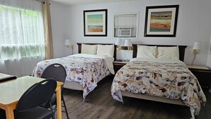 Habitación de hotel con dos camas, un escritorio, una silla y dos cuadros en la pared.