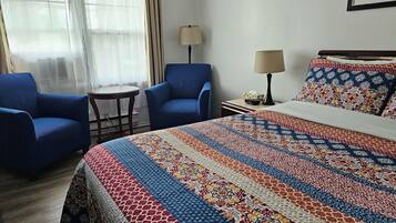 Habitación de hotel con una cama grande, dos sillones azules, una mesita redonda y una lámpara.