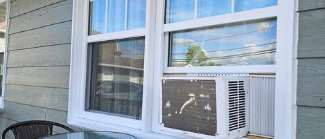 A covered patio with a table and two chairs, a window with a view of the sky, and an air conditioning unit.
