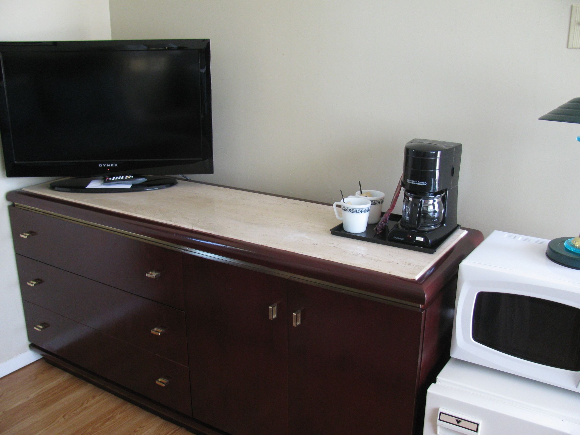 A hotel room with a television, coffee maker, microwave, and a cabinet with drawers.