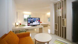 Un salon moderne avec un téléviseur à écran plat, un canapé, une petite table ronde et un pouf à rayures.