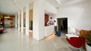 Un hall d’hôtel moderne avec un comptoir d’accueil, un coin salon avec un fauteuil rouge et une plante.