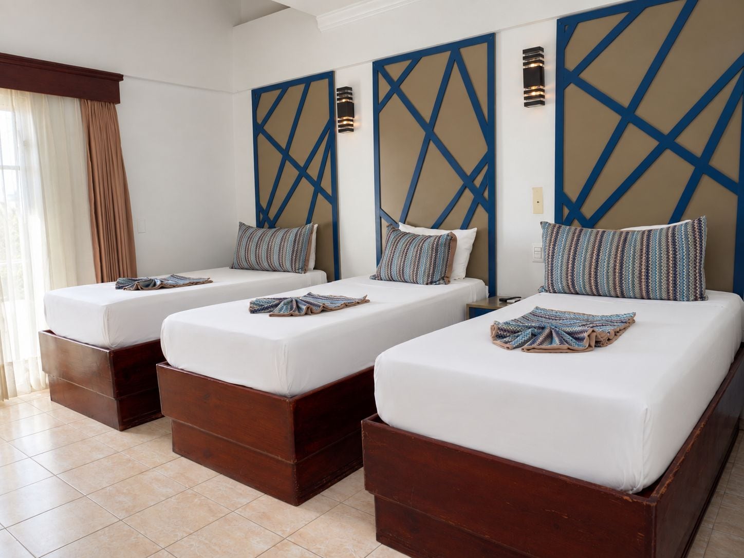 Una habitación de hotel con tres camas dispuestas en fila, cada una con estructura de madera y ropa blanca.