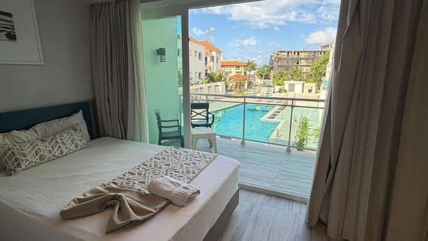 Una habitación de hotel con cama, vista a una piscina y balcón.