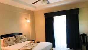 Una habitación de hotel con cama, ventilador de techo, mesita de noche y una silla.