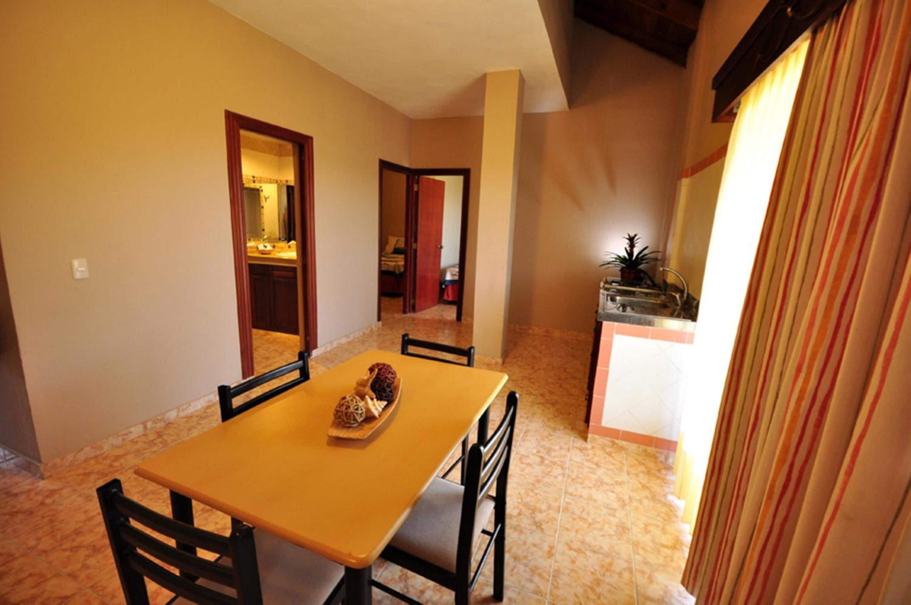 A dining area with a table and chairs, a kitchen visible through an open door, and a striped curtain.
