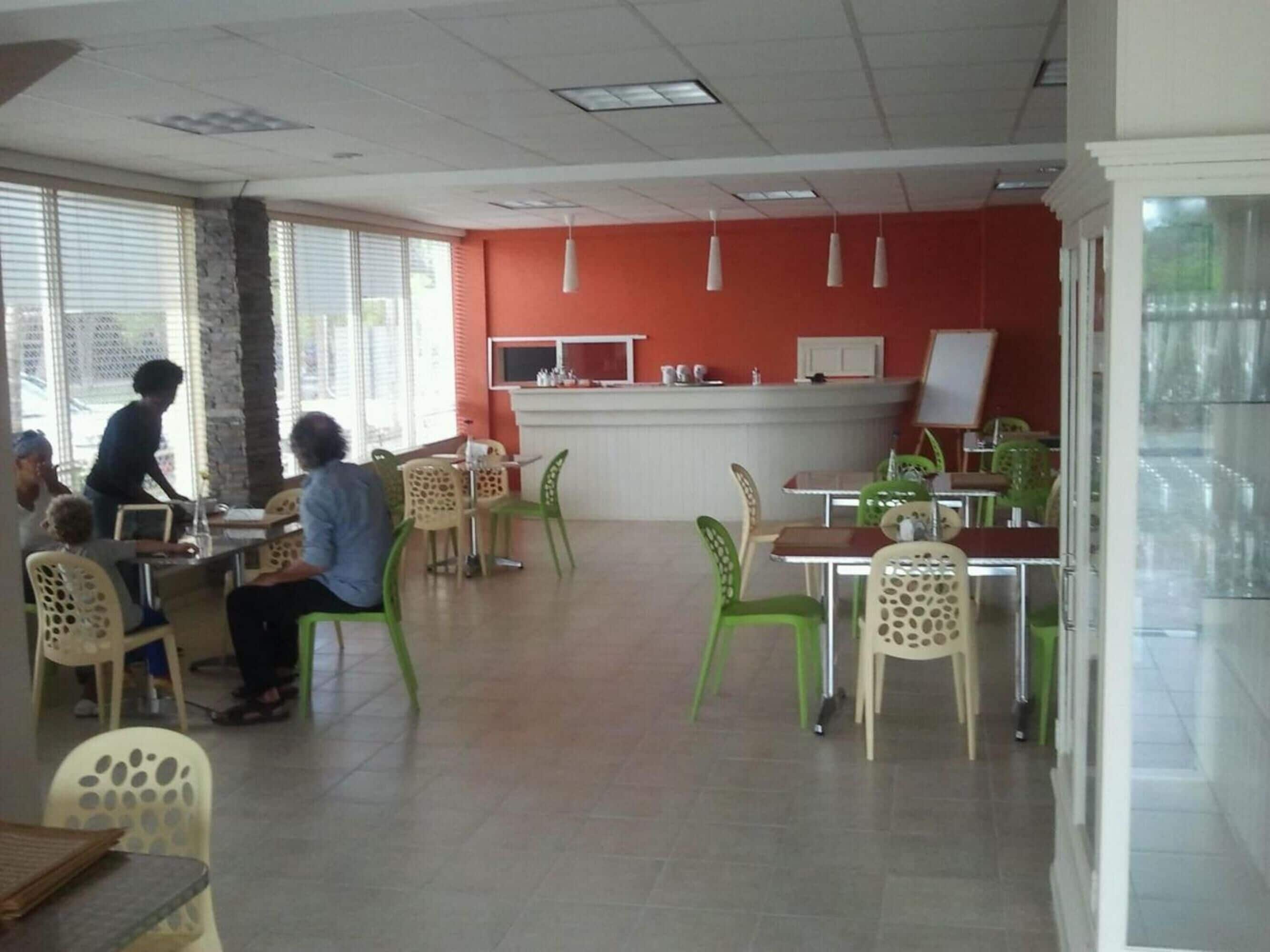 Un espace repas avec des tables et des chaises, un comptoir avec un tableau blanc et une personne qui sert les plats.