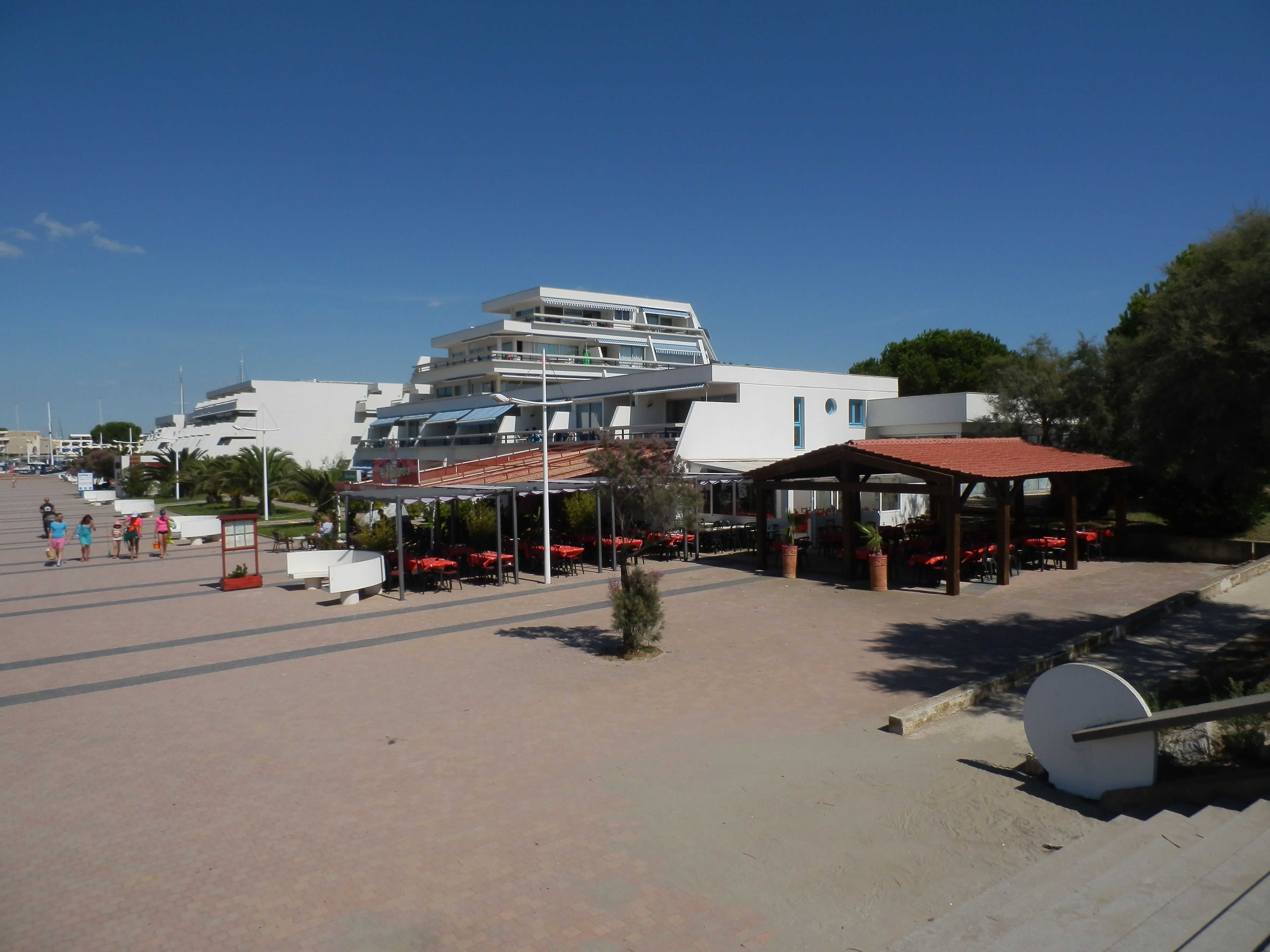 Una zona frente a la playa con un edificio moderno, asientos al aire libre y un área techada.