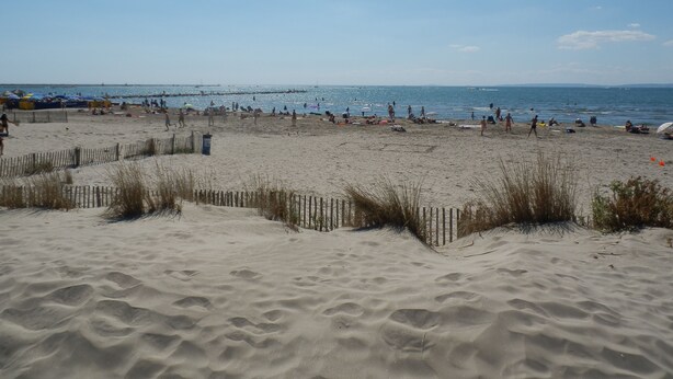 A sandy beach with a wooden fence and people in the distance. - Les Rivages d'Ulysse (Le Grau-Du-Roi)