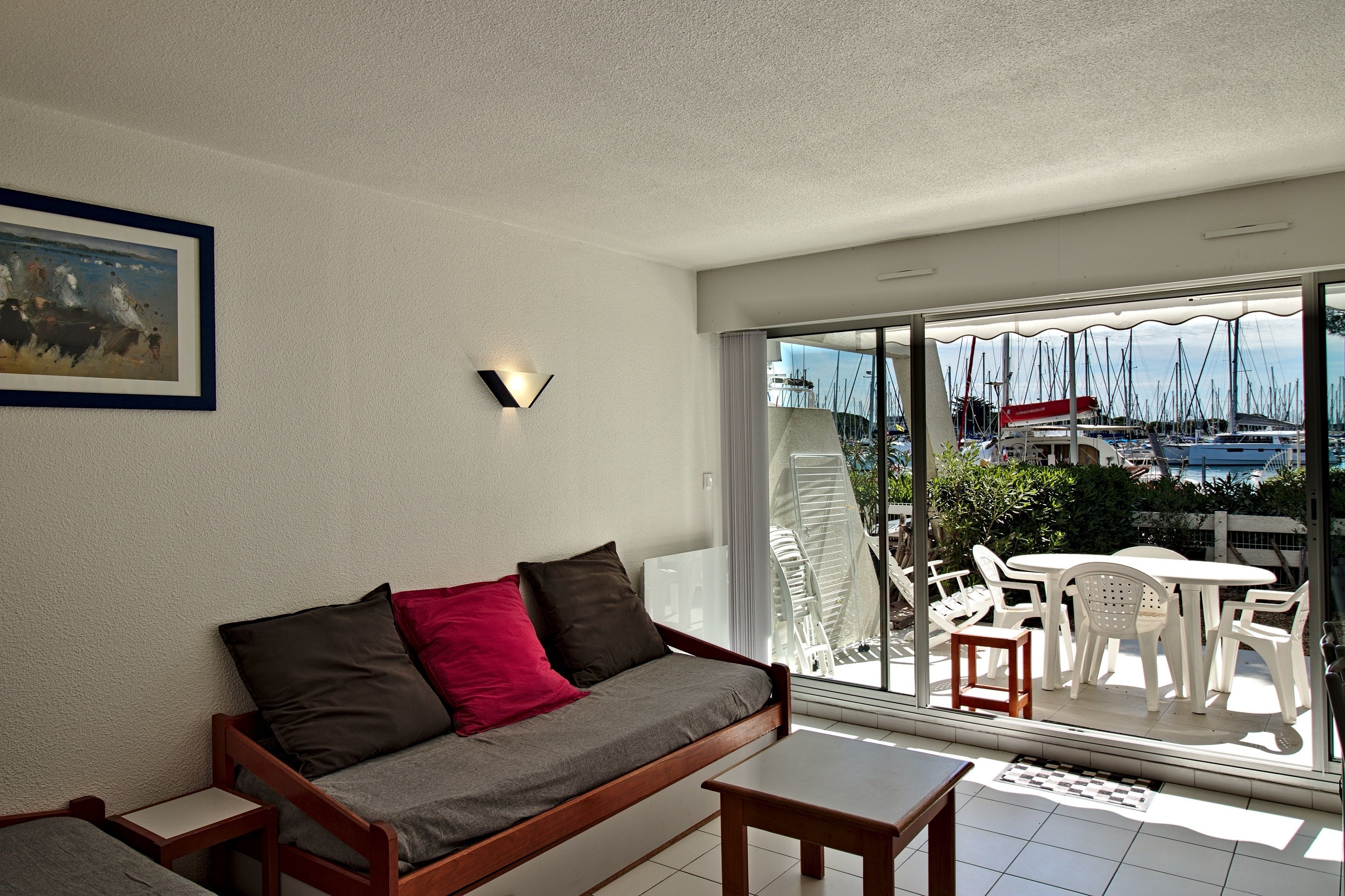 A balcony with a sofa, table, and chairs, overlooking a marina with boats.