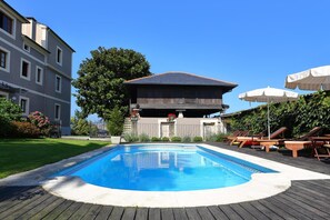 Una piscina con muelle de madera, sillas de descanso y sombrillas.
