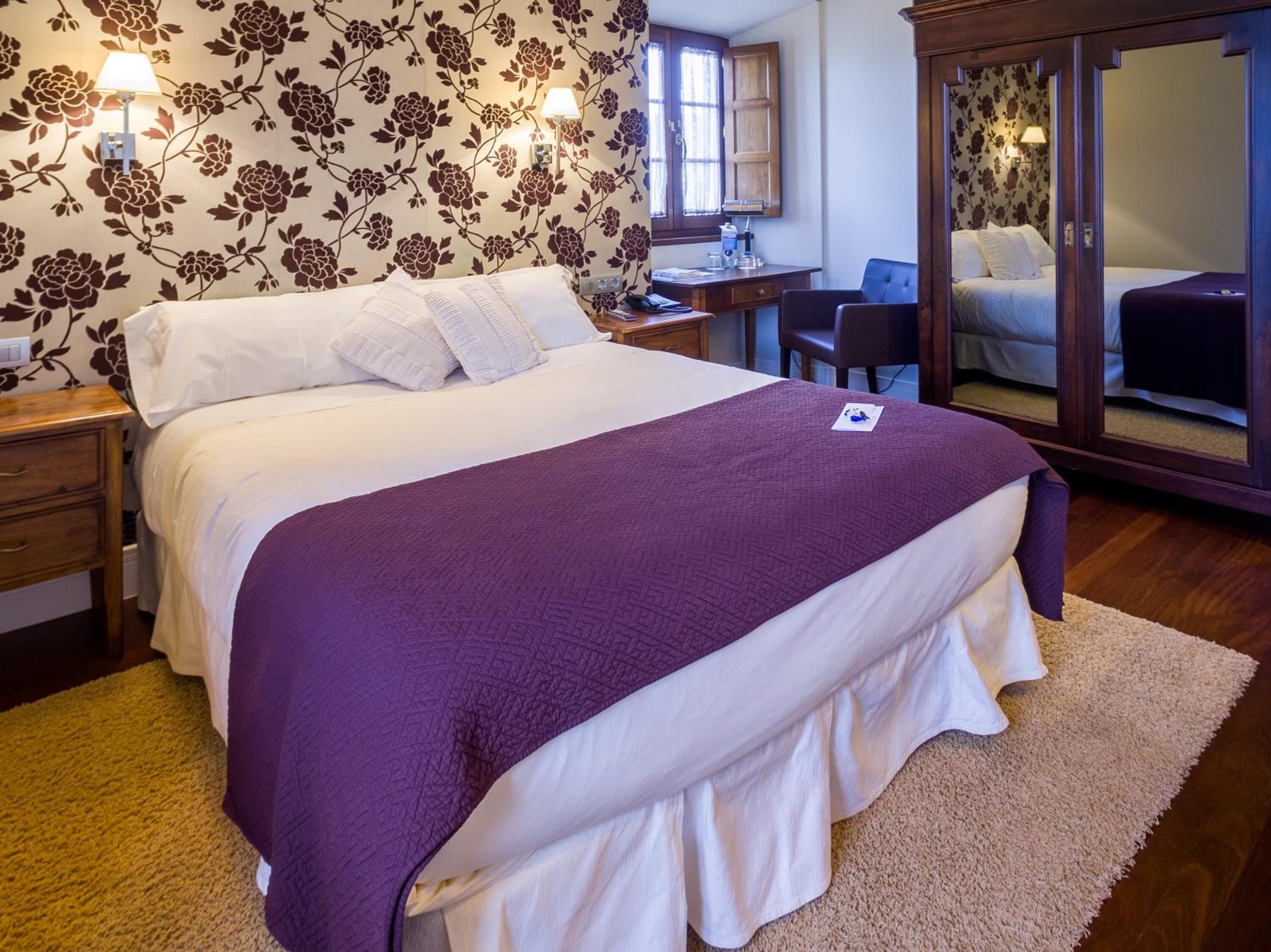 A bedroom with a large bed, a desk, a chair, and a wardrobe.