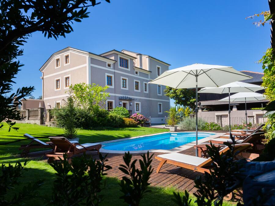 A swimming pool with lounge chairs and umbrellas, surrounded by a well-maintained lawn and a multi-story building in the background.